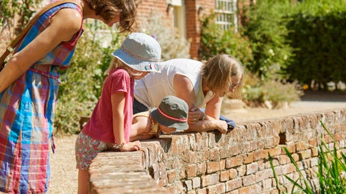 Visitors looking over a low wall down towards the river at Flatford Mill, at Flatford, Suffolk